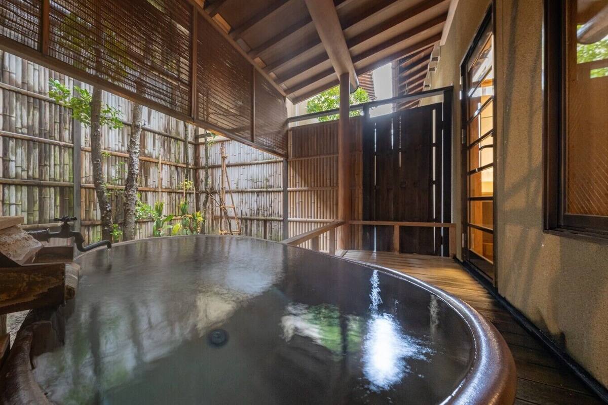 A traditional Japanese onsen with a wooden interior, a hot spring bath, and a bamboo fence.