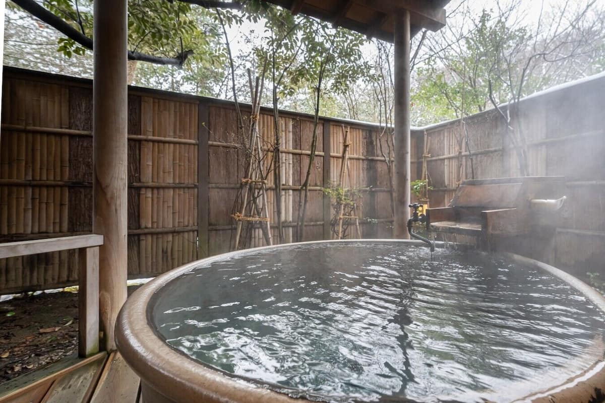 A hot spring with a wooden deck and bamboo fence in the background.
