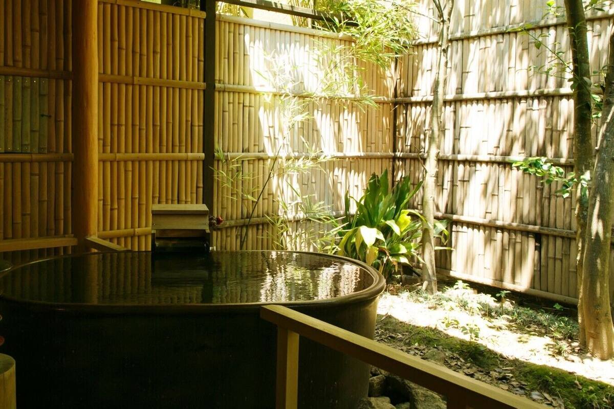 A tranquil outdoor area with a water feature, bamboo walls, and a small table with a lantern.