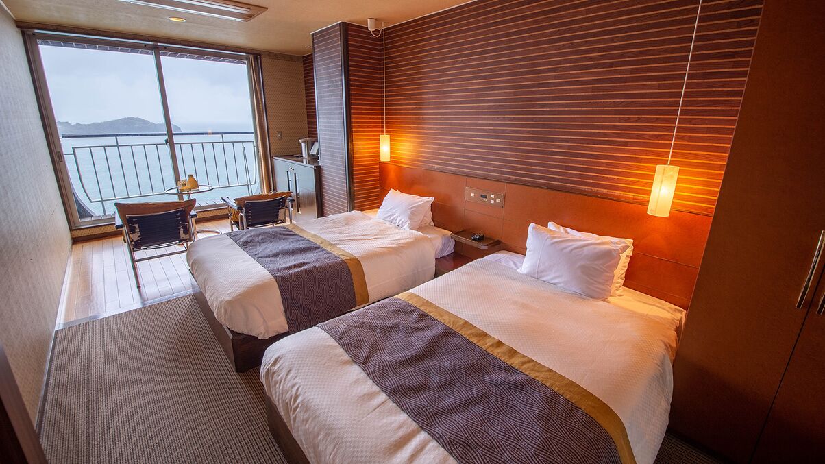 Habitación de hotel con dos camas, un balcón con vistas y un escritorio con una silla.