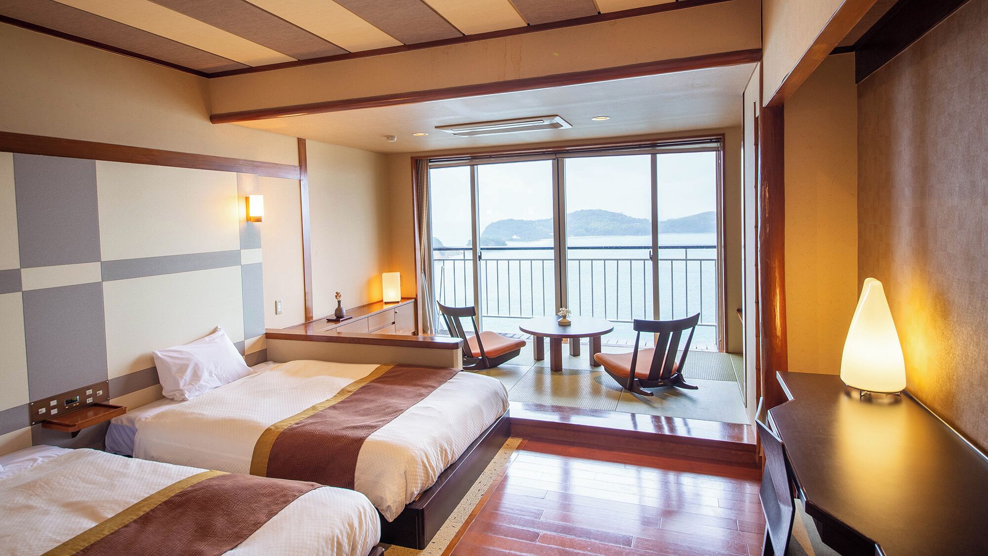 Habitación de hotel con dos camas, un balcón con mesa y sillas, y vista al mar.