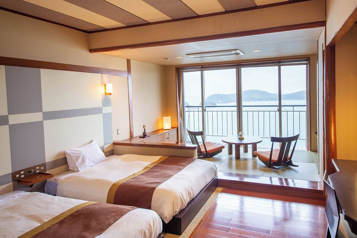 A hotel room with two beds, a balcony with a table and chairs, and a view of the sea.