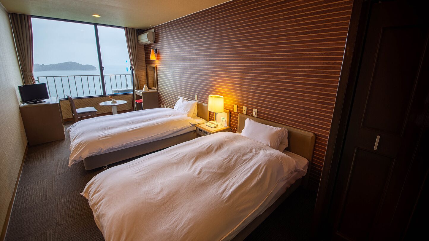 Habitación de hotel con dos camas, una mesita, una silla, televisión y ventana con vistas.
