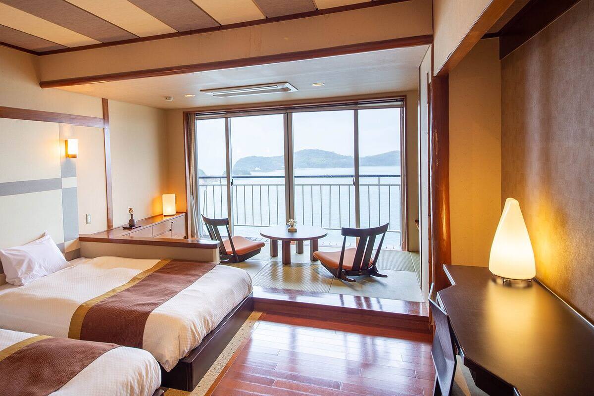 A hotel room with two beds, a balcony with a view, a small table, and a chair.