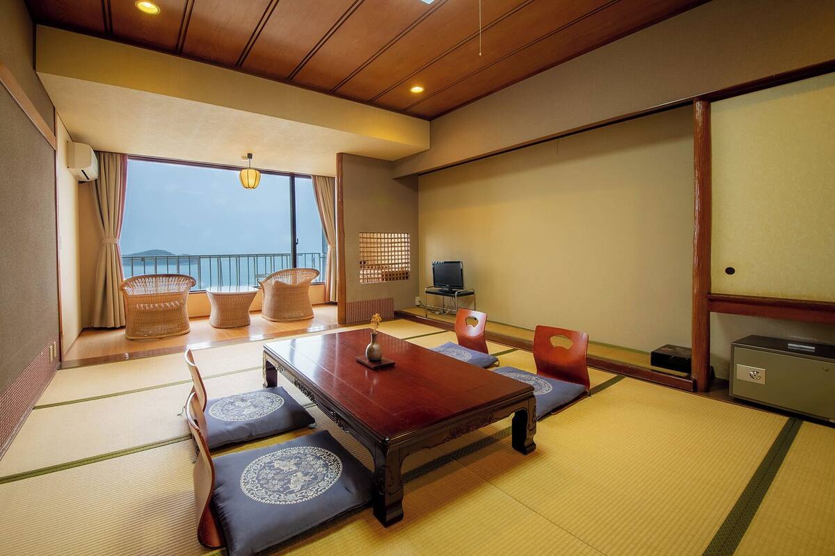 A traditional Japanese room with tatami flooring, a low wooden table, and a view of the sea.
