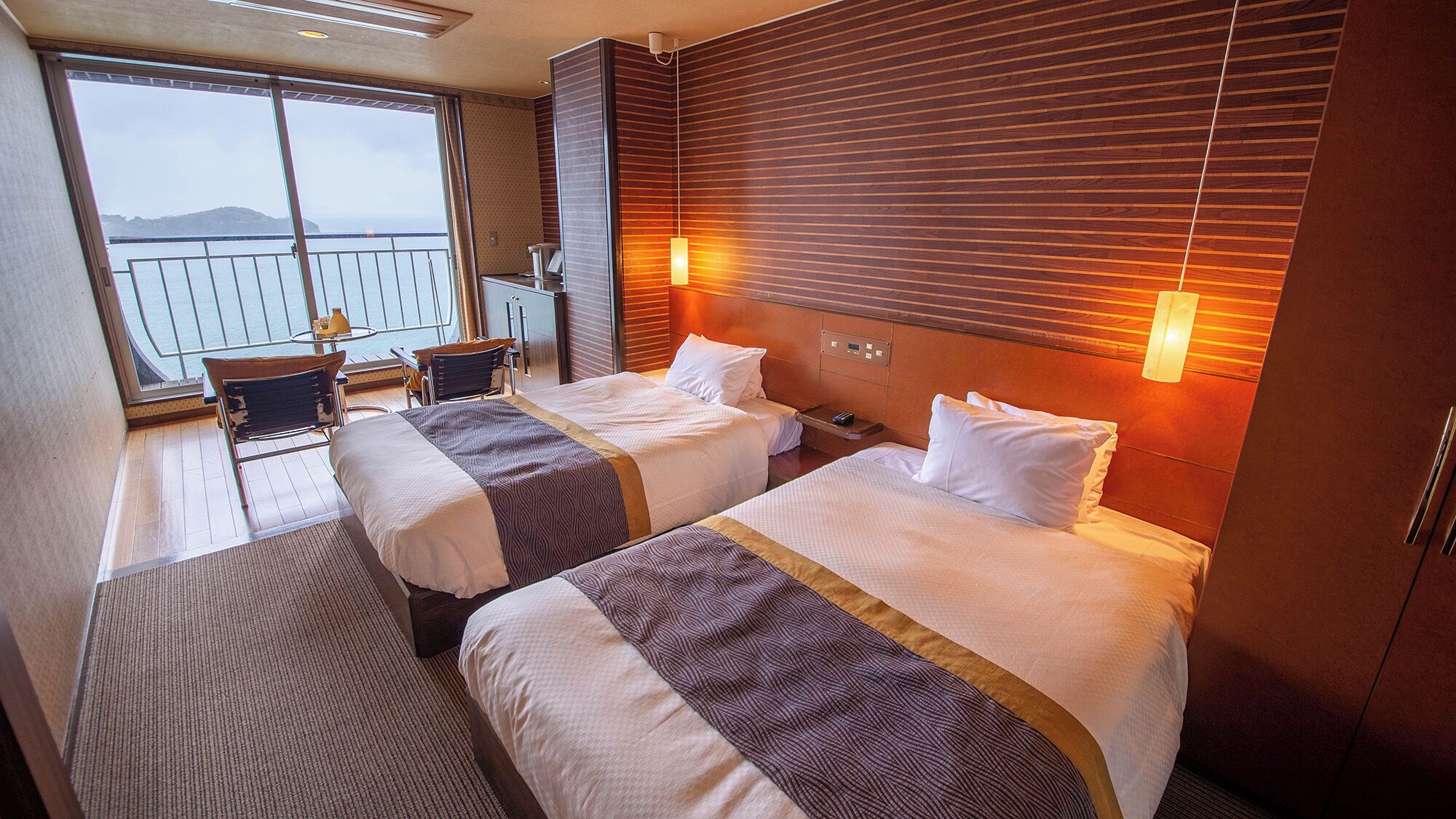 Habitación de hotel con dos camas, un balcón con vistas y una pequeña zona de estar.