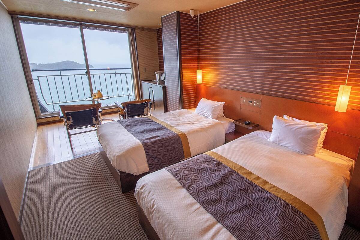A hotel room with two beds, a balcony with a view, and a small seating area.