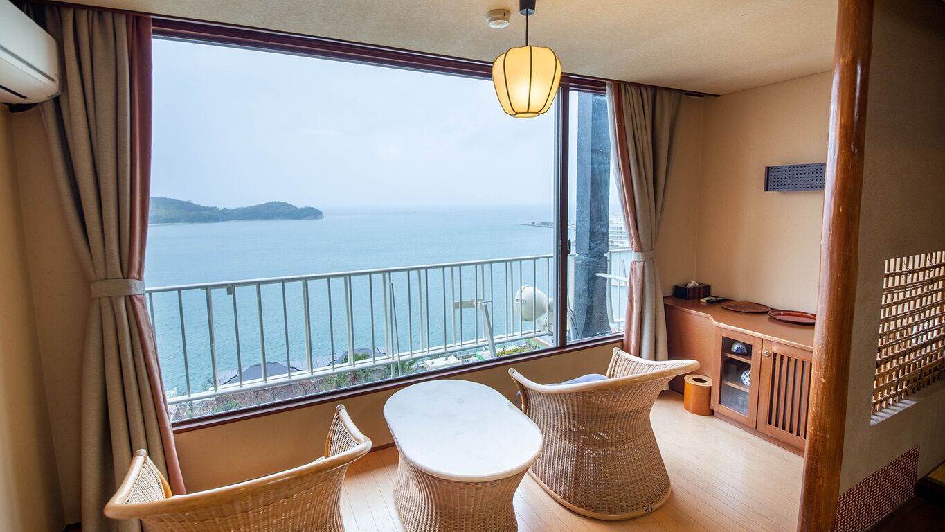 Un balcón con vistas al mar, mobiliario de mimbre y una pequeña mesa.