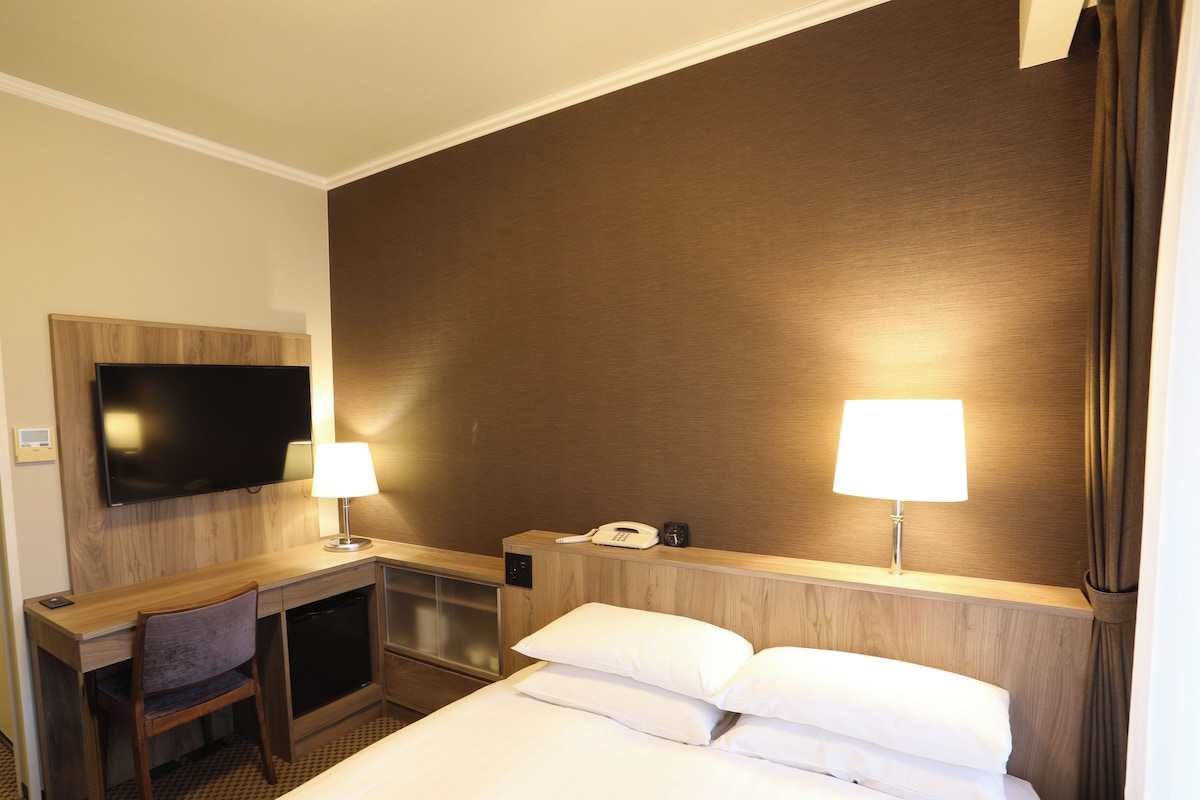 Una habitación de hotel con cama, escritorio, silla, televisor, lámparas y teléfono.
