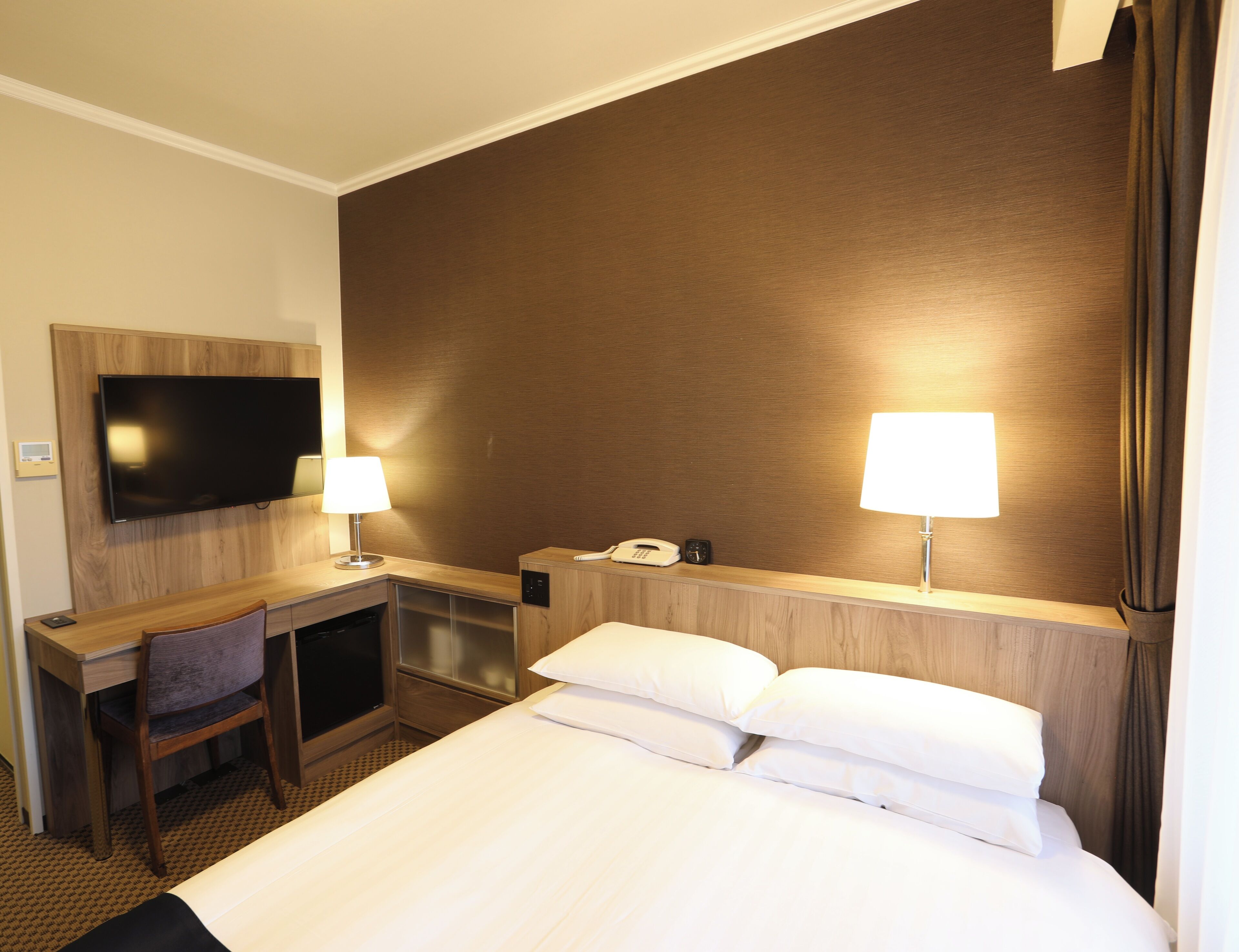 Una habitación de hotel con cama, escritorio, silla, televisor, lámparas y teléfono.