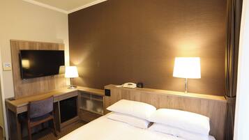 A hotel room with a bed, desk, chair, TV, lamps, and a phone.