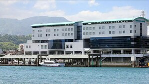 Um edifício moderno com vários andares, uma área à beira-mar coberta e um barco atracado em primeiro plano.