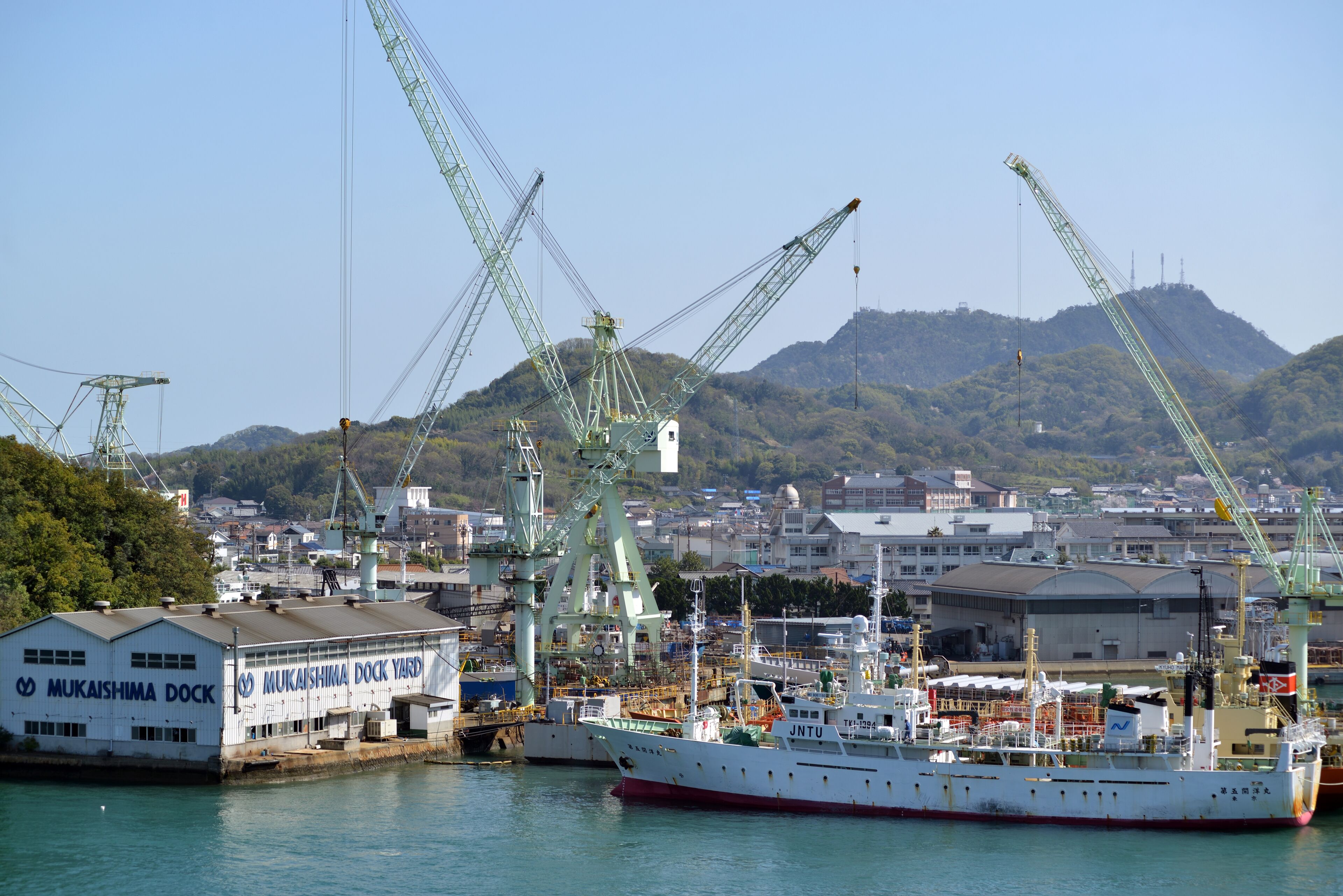 A large cargo ship docked at a port with cranes and industrial buildings in the background.