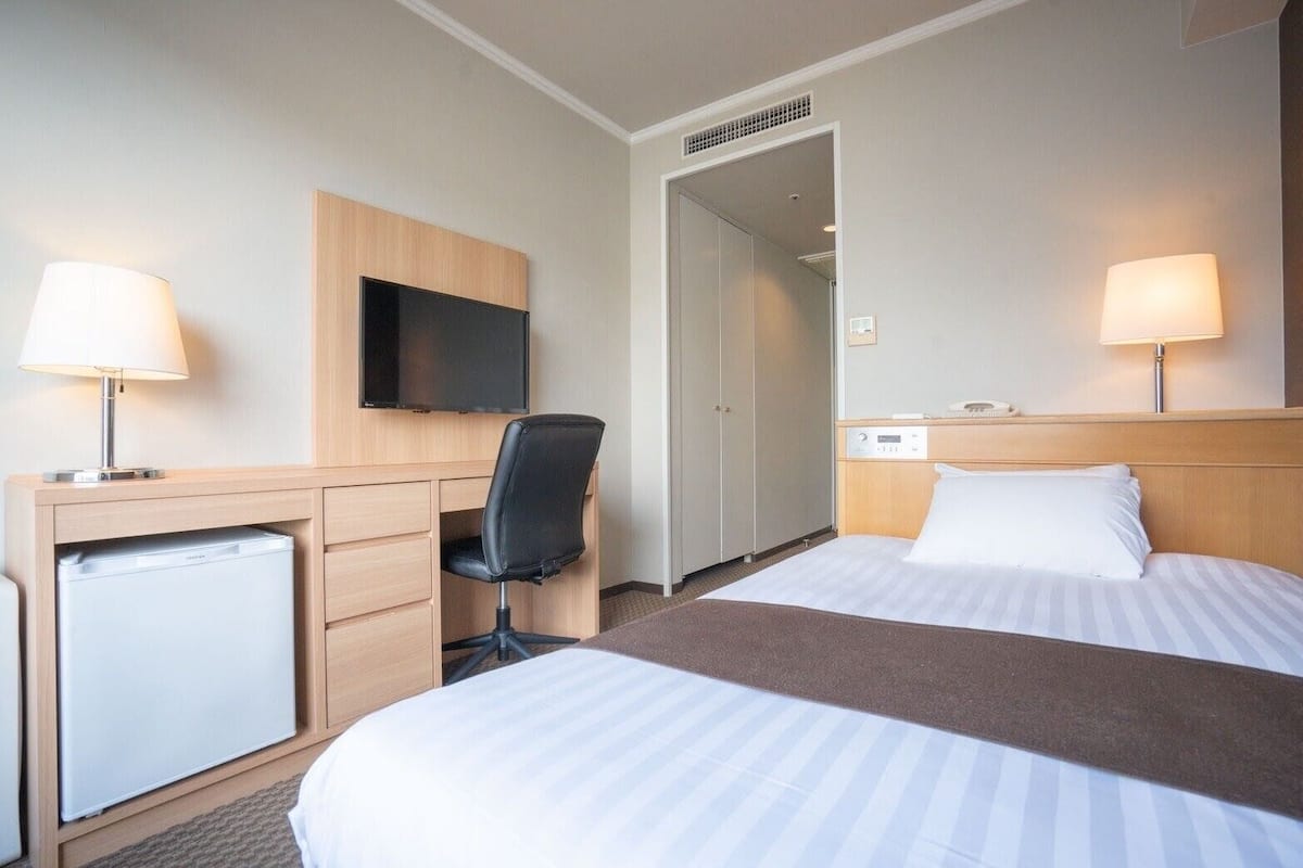 A hotel room with two beds, a desk with a chair, a television, and a minibar.