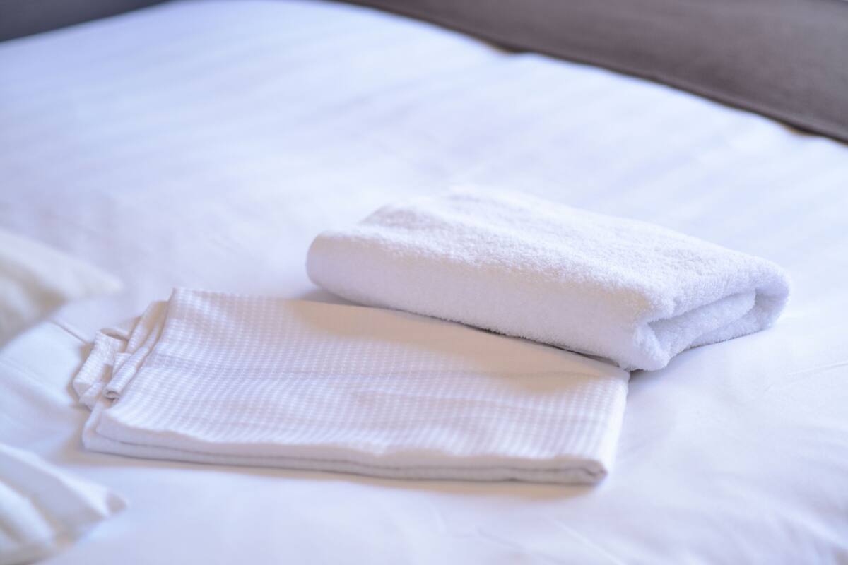 A neatly made bed with white linens and a folded towel.