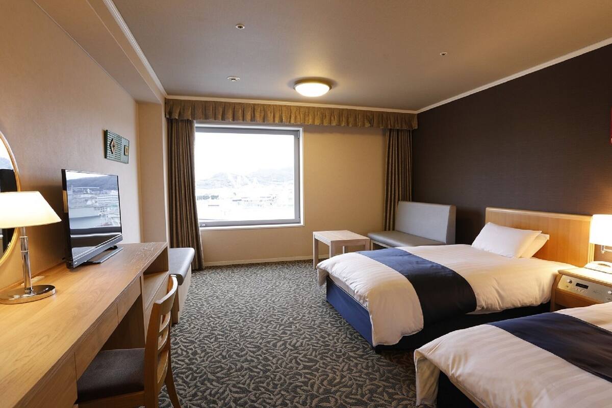 A hotel room with a bed, desk, chair, and a TV.