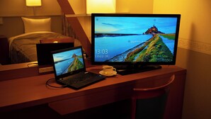 Ein Hotelzimmer mit einem Holztisch, einem Laptop, einem Desktop-Monitor und einer Kaffeetasse.