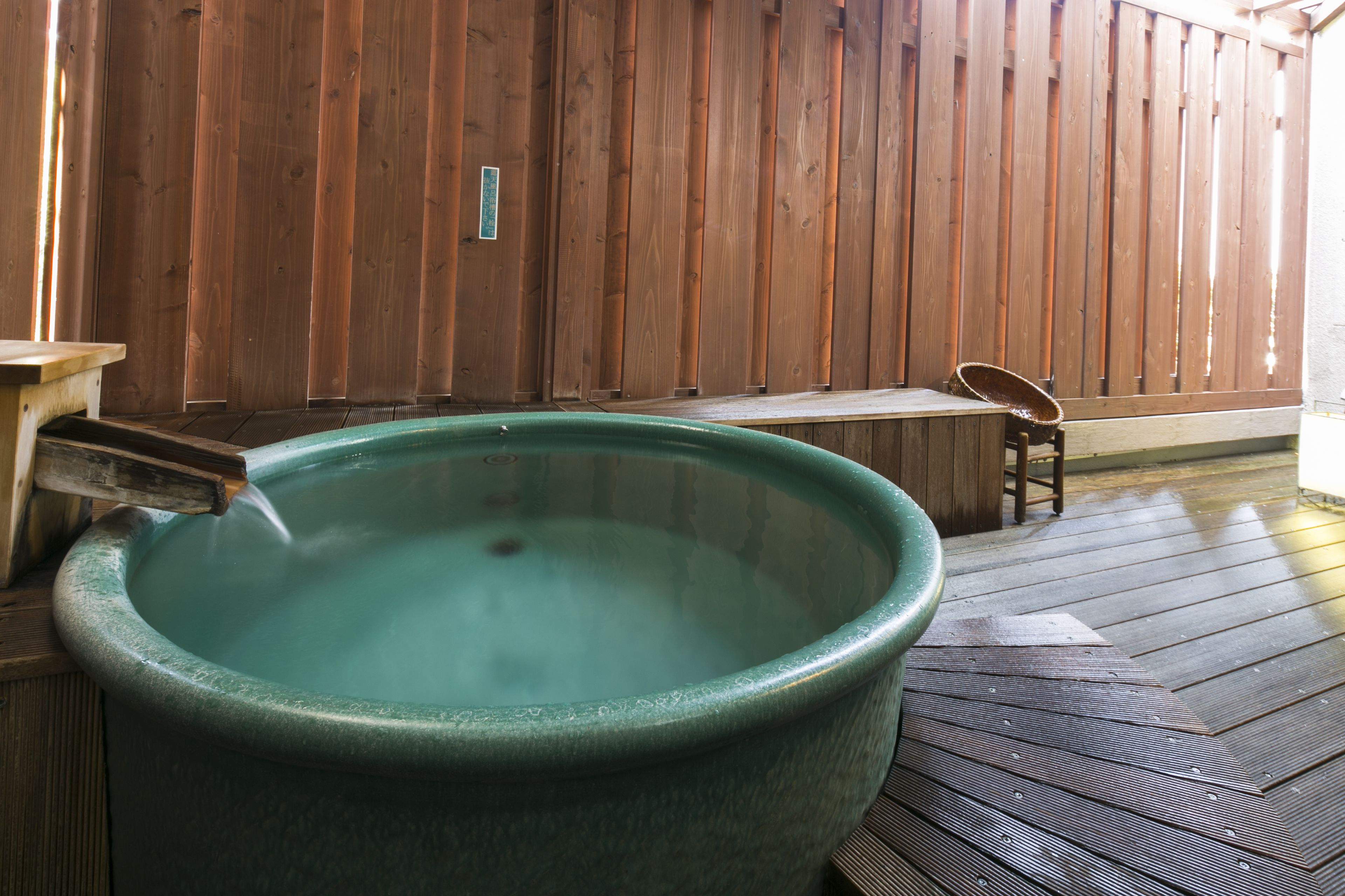 Un jacuzzi grande y redondo, de color verde, en una habitación con suelo y pared de madera, y un banco.