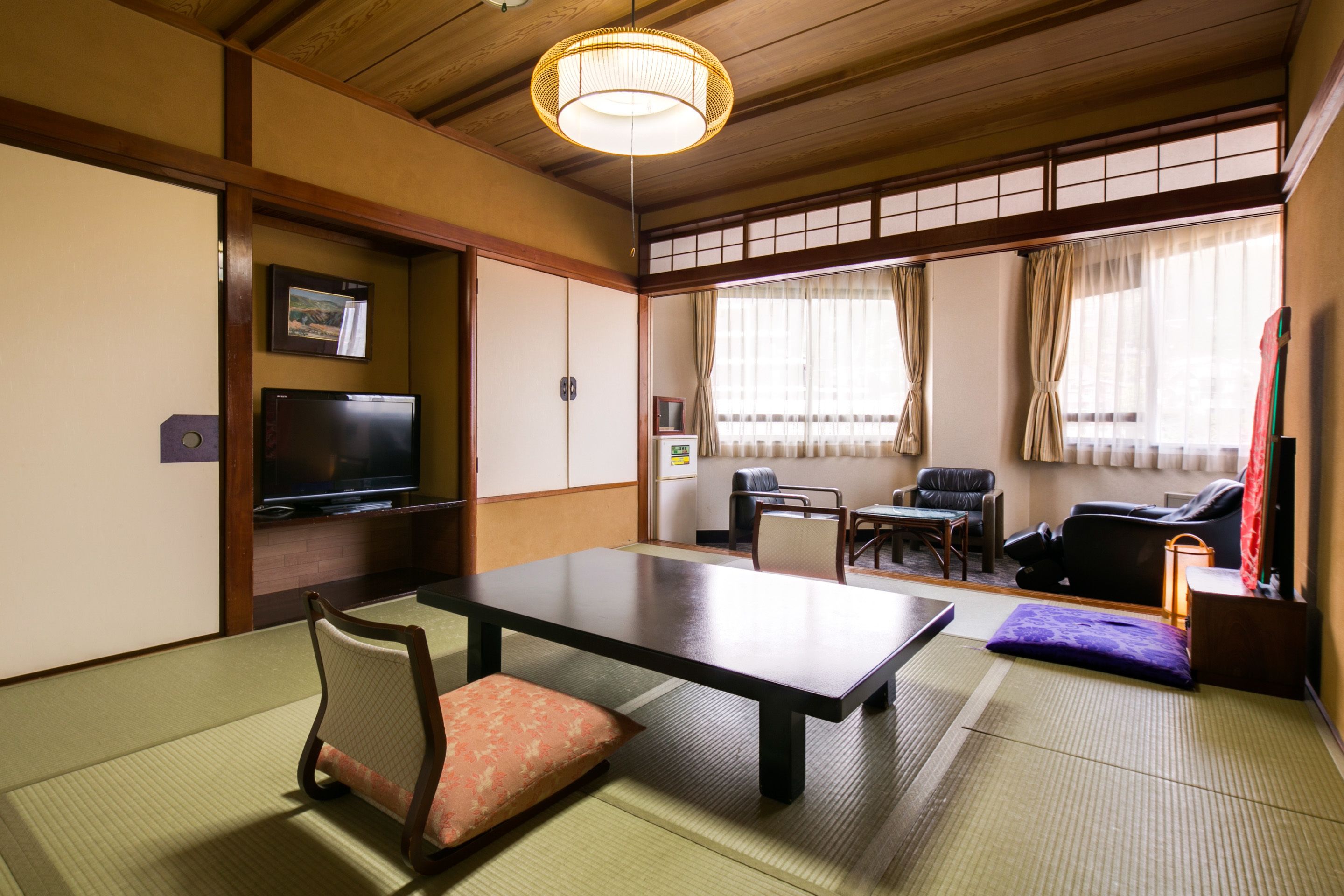 Una habitación japonesa tradicional con suelo de tatami, una mesa baja, un televisor y puertas correderas.