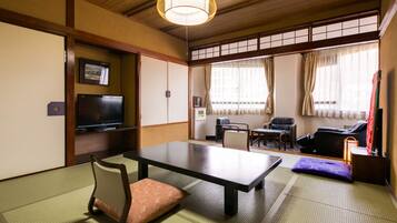 Una habitación japonesa tradicional con suelo de tatami, una mesa baja, un televisor y puertas correderas.