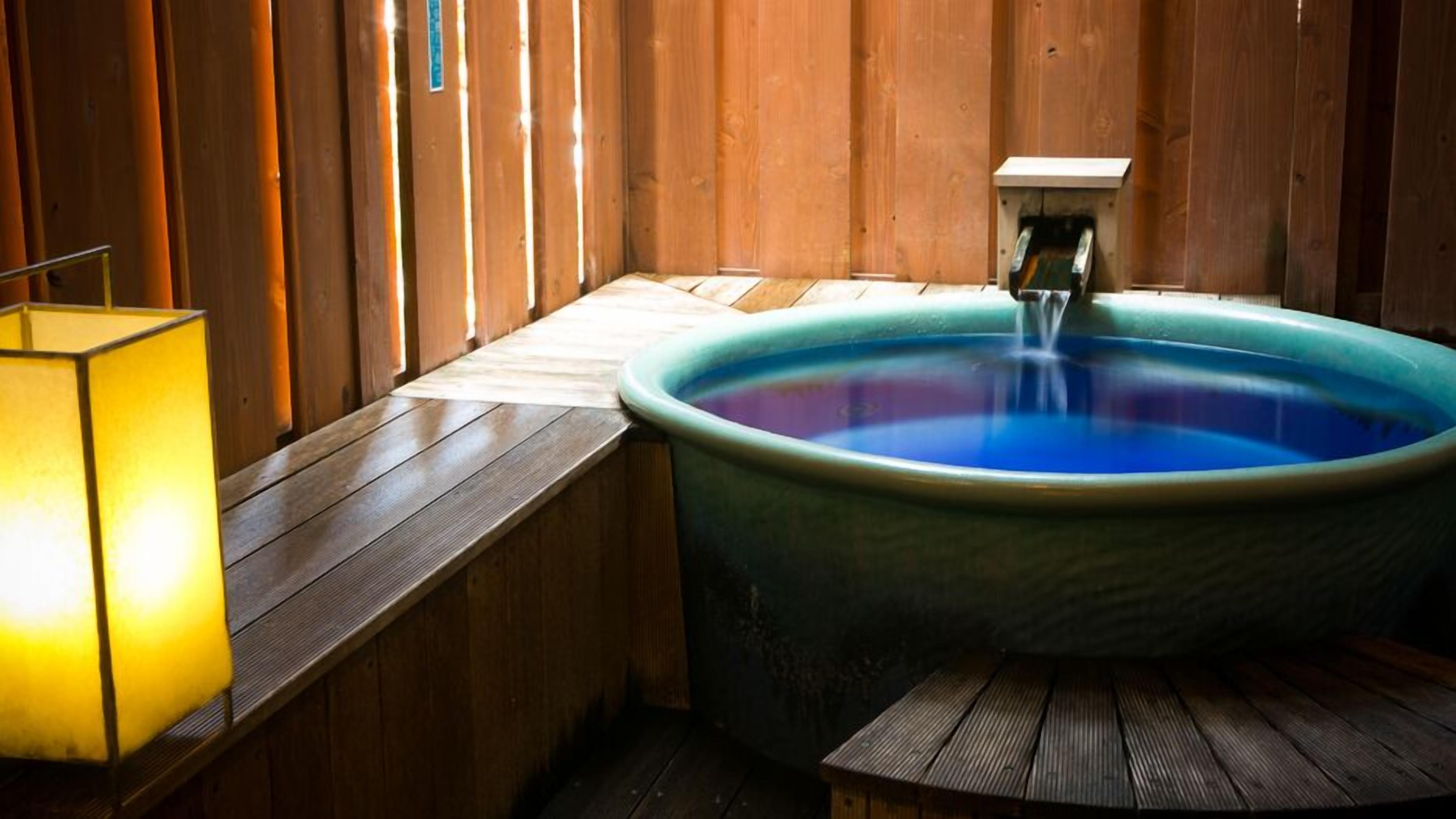A wooden room with a large bathtub, a bench, and a wall-mounted light fixture.