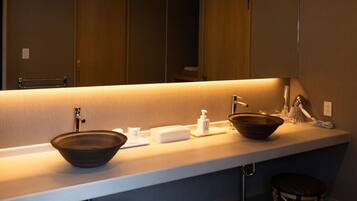 A modern bathroom with a large mirror, two sinks, a soap dispenser, and a towel rack.