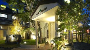 A hotel entrance with a stone pathway leading to the door, surrounded by greenery and illuminated by ambient lighting. - Kawaguchiko Park Hotel (FUJIKAWAGUCHIKO)