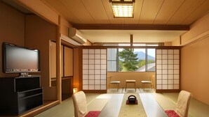 A traditional Japanese room with tatami flooring, a low table, two chairs, a television, and a view of a mountain through shoji screens. - Kawaguchiko Park Hotel (FUJIKAWAGUCHIKO)