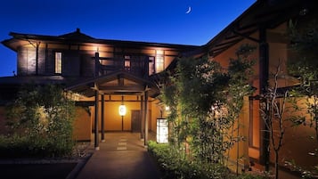 A traditional Japanese building with a wooden exterior, a covered entrance, and a small garden area with plants.
