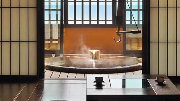 Una habitación japonesa tradicional con suelo de tatami, un baño termal y vistas al mar a través de un puertas correderas.