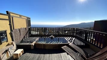 A wooden deck with a hot tub, seating, and a view of the mountains.