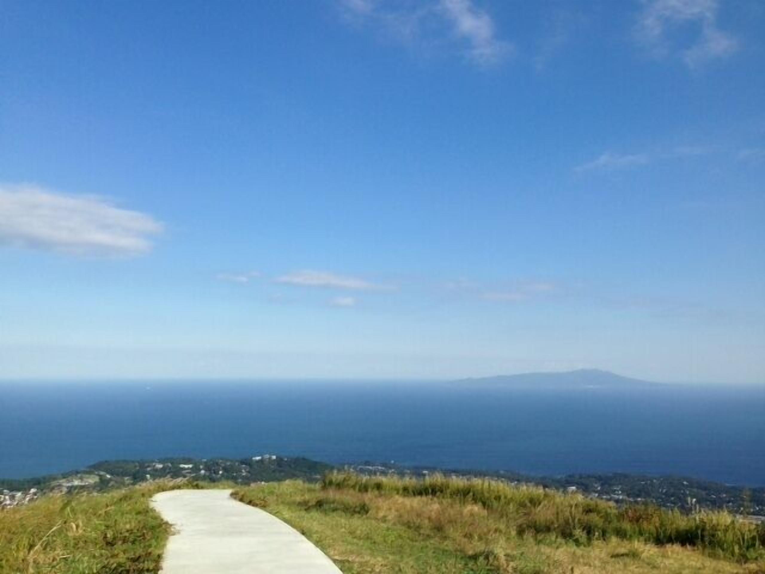 A paved pathway leading to a scenic overlook with a view of the ocean and distant land.