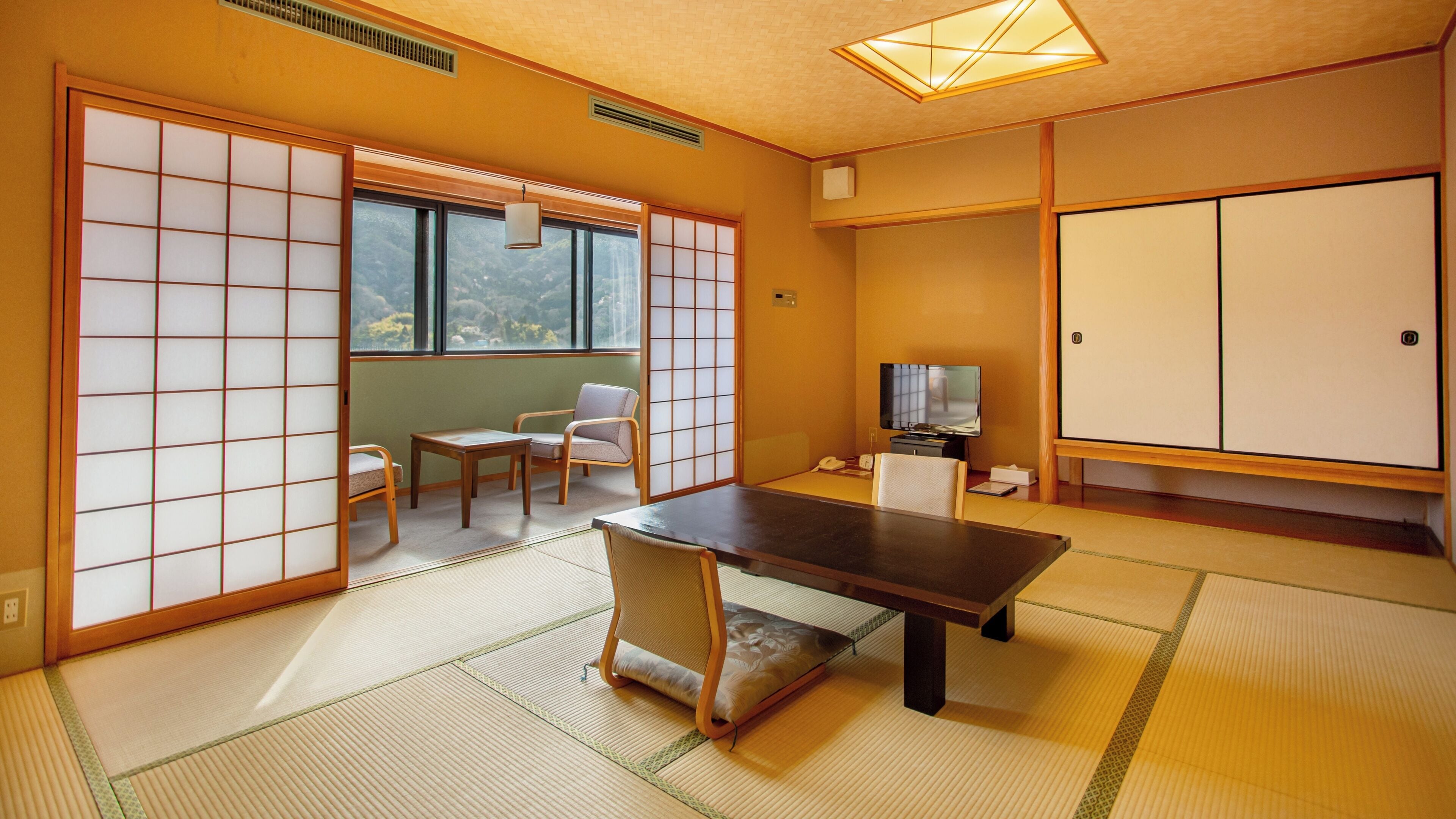 A traditional Japanese room with tatami flooring, a low table, a television, and sliding doors.