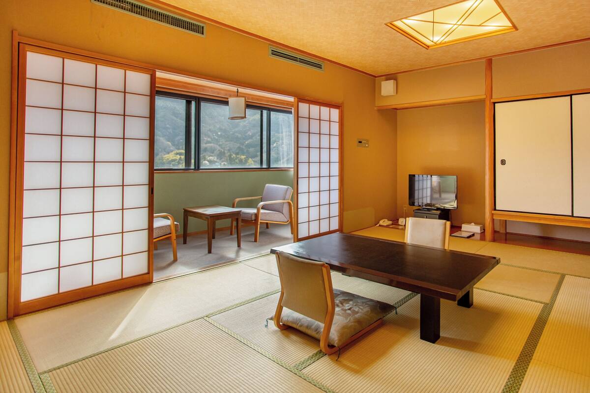 Una habitación japonesa tradicional con suelo de tatami, una mesa baja, un televisor y puertas correderas.