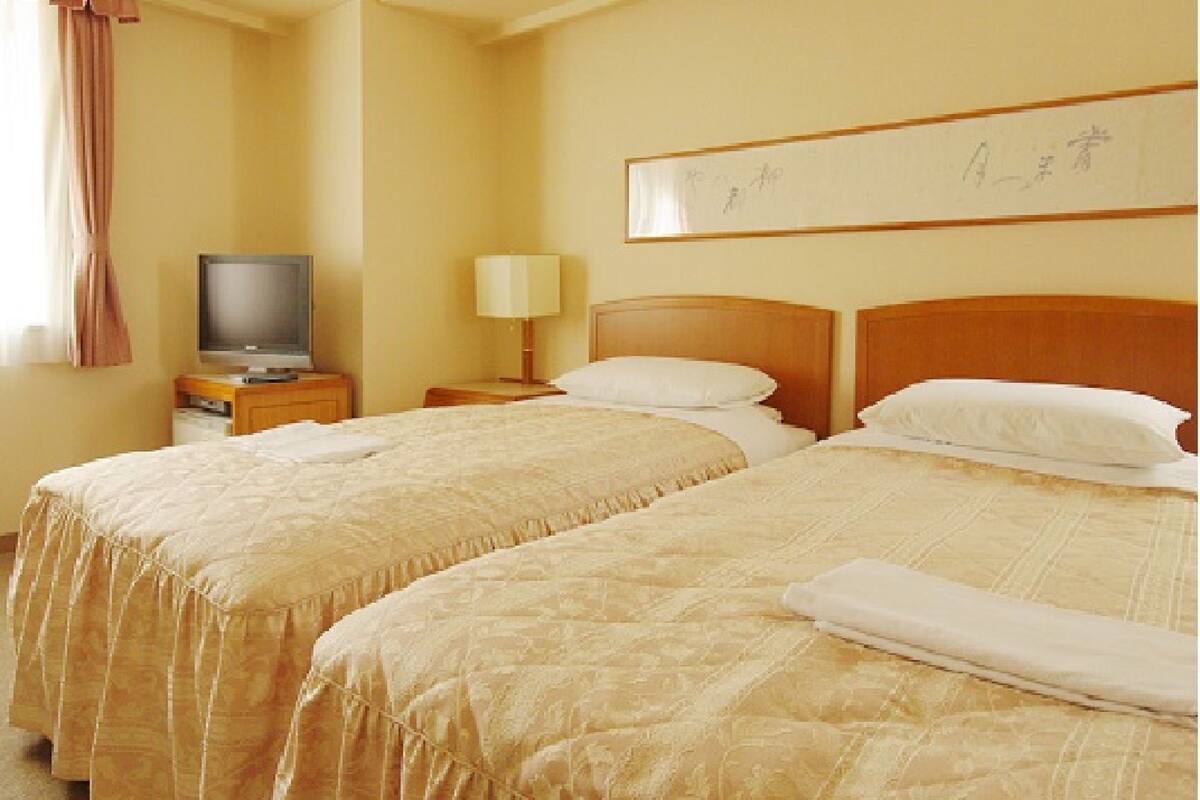 A hotel room with two beds, a television on a nightstand, and a lamp.