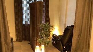 Une pièce avec un sol à carreaux, un fauteuil en cuir noir, une plante dans un vase blanc et une fenêtre ornée de rideaux à motifs.