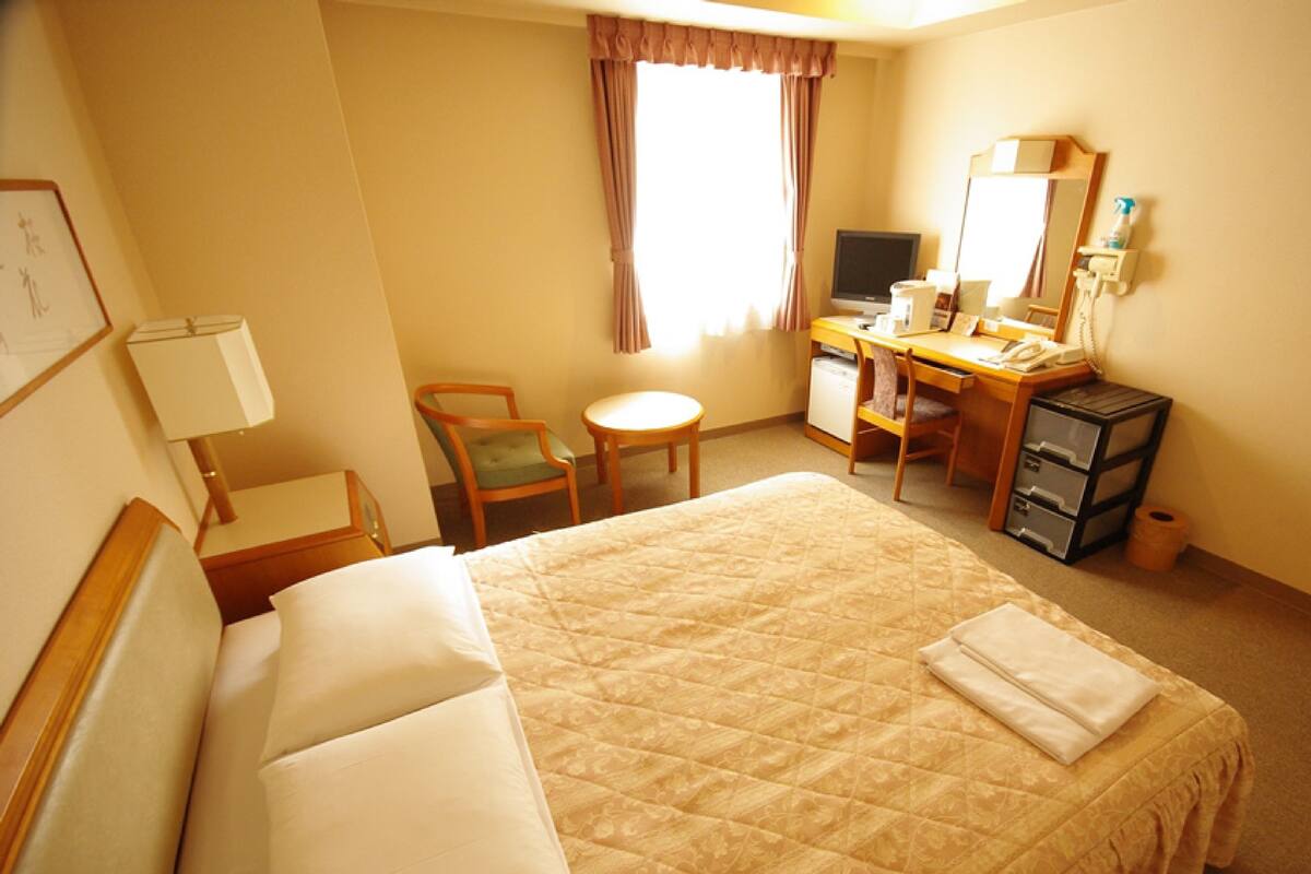 A hotel room with a large bed, a desk with a computer, a chair, a small table, and a mirror.