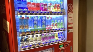 Un distributeur automatique proposant diverses boissons et collations, un four à micro-ondes et un panneau indiquant que le paiement par Coca-Cola est accepté.