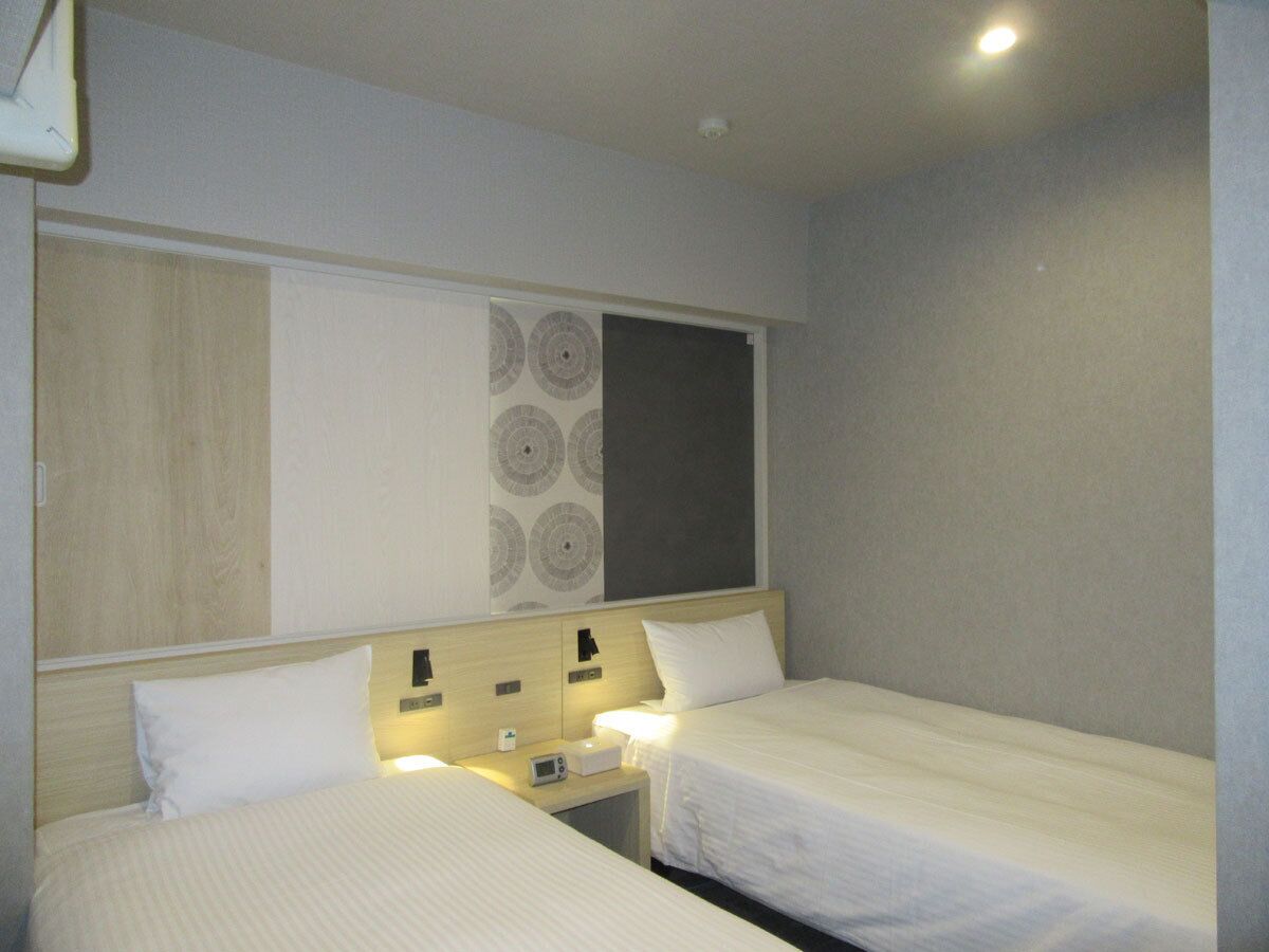 Una habitación de hotel con dos camas individuales, mesitas de noche, un reloj de pared y una lámpara en el techo.