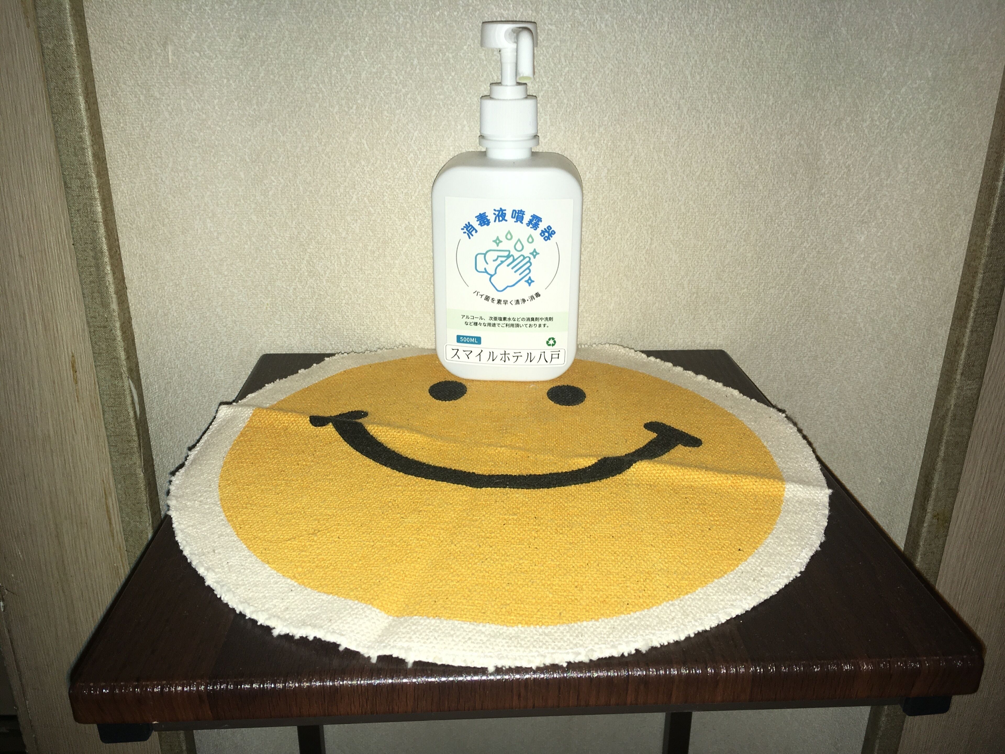 A bottle of hand sanitizer on a table with a smiley face cloth.
