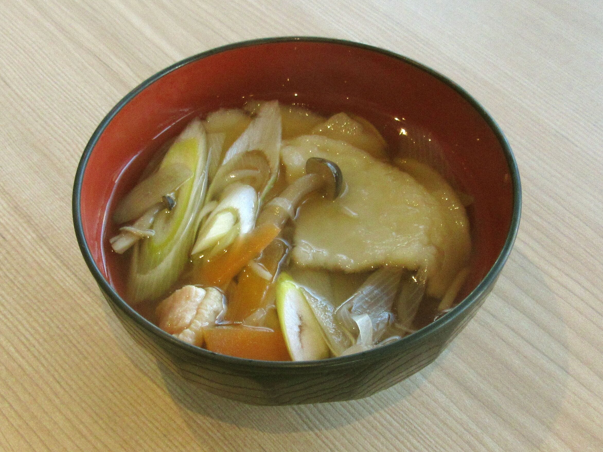 En skål med soppa, olika grönsaker och en klar buljong.