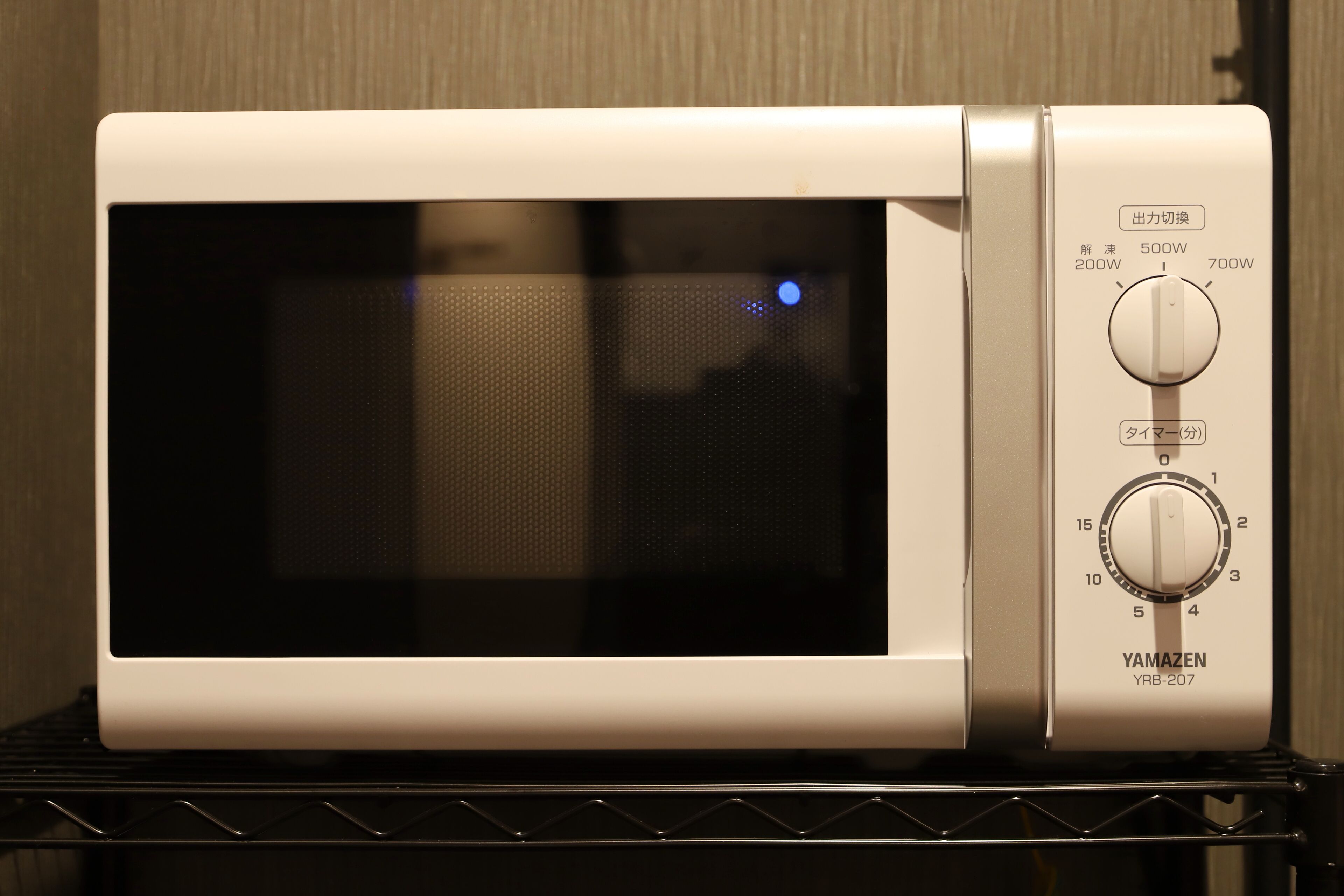 Un four à micro-ondes blanc, doté d’un écran numérique et de boutons de commande, posé sur une étagère en métal.
