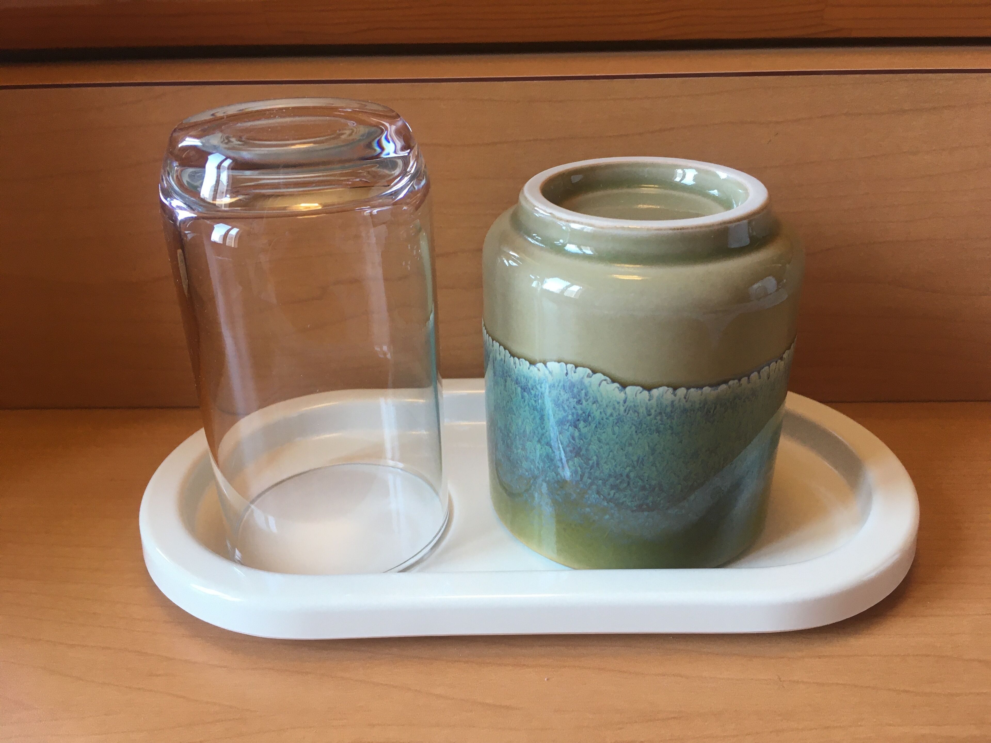 A clear glass jar and a ceramic pot on a white tray.