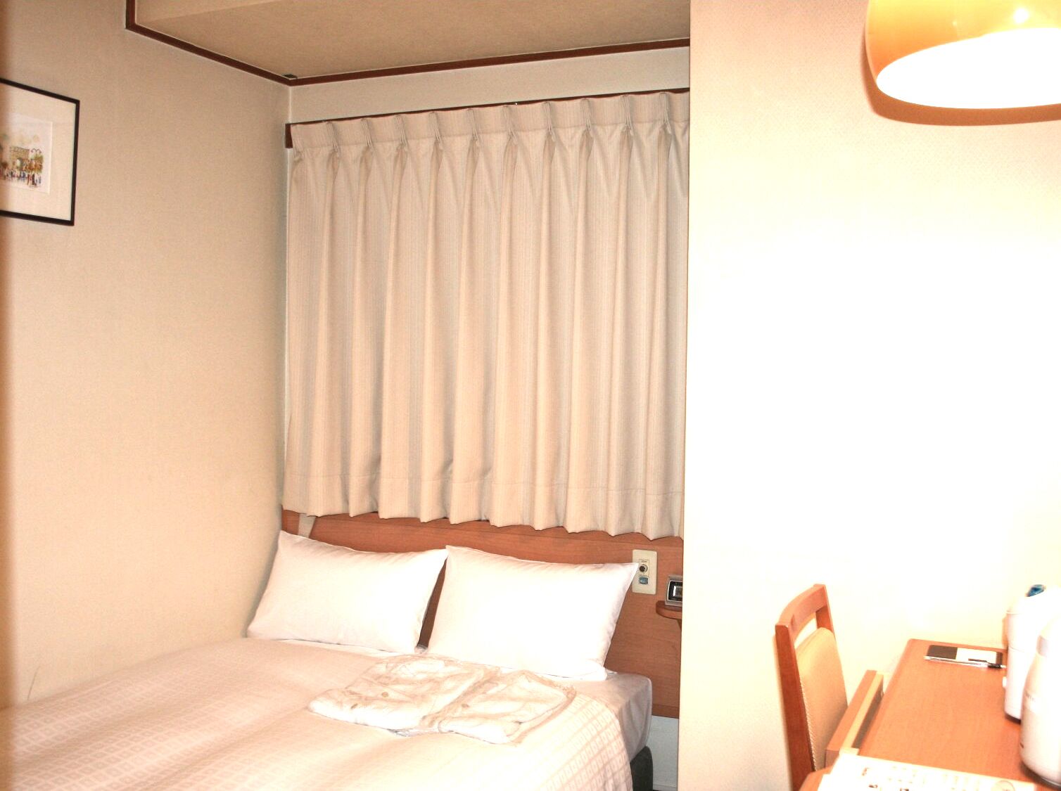 Ein Hotelzimmer mit Bett, Kissen, Nachttisch und Vorhang.