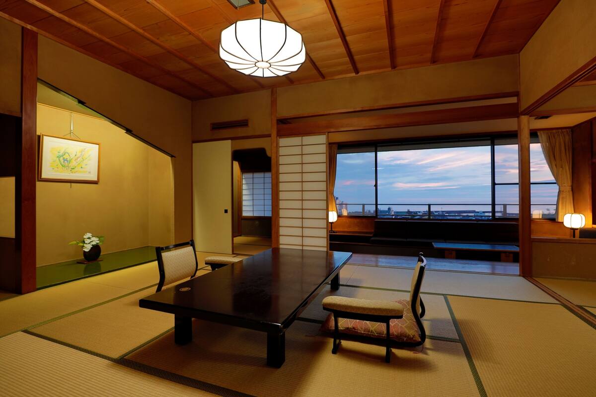 Ein traditioneller japanischer Raum mit Tatami-Böden, einem niedrigen Tisch und Blick auf die Stadt durch große Fenster.