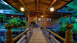 Un puente de madera con barandillas que conduce a un edificio tradicional con tejado de azulejos y faroles.