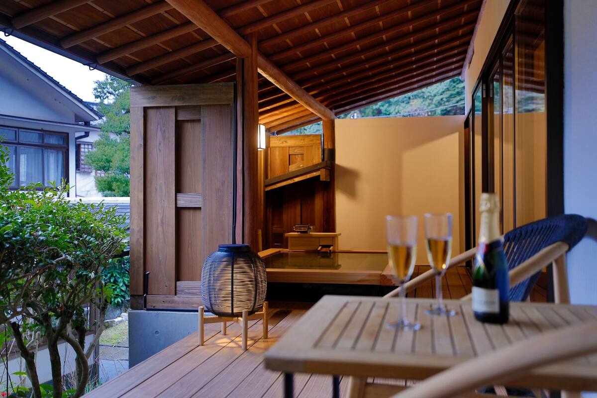 Eine Holzterrasse mit Tisch und Stühlen, einer Champagnerflasche und zwei Gläsern.