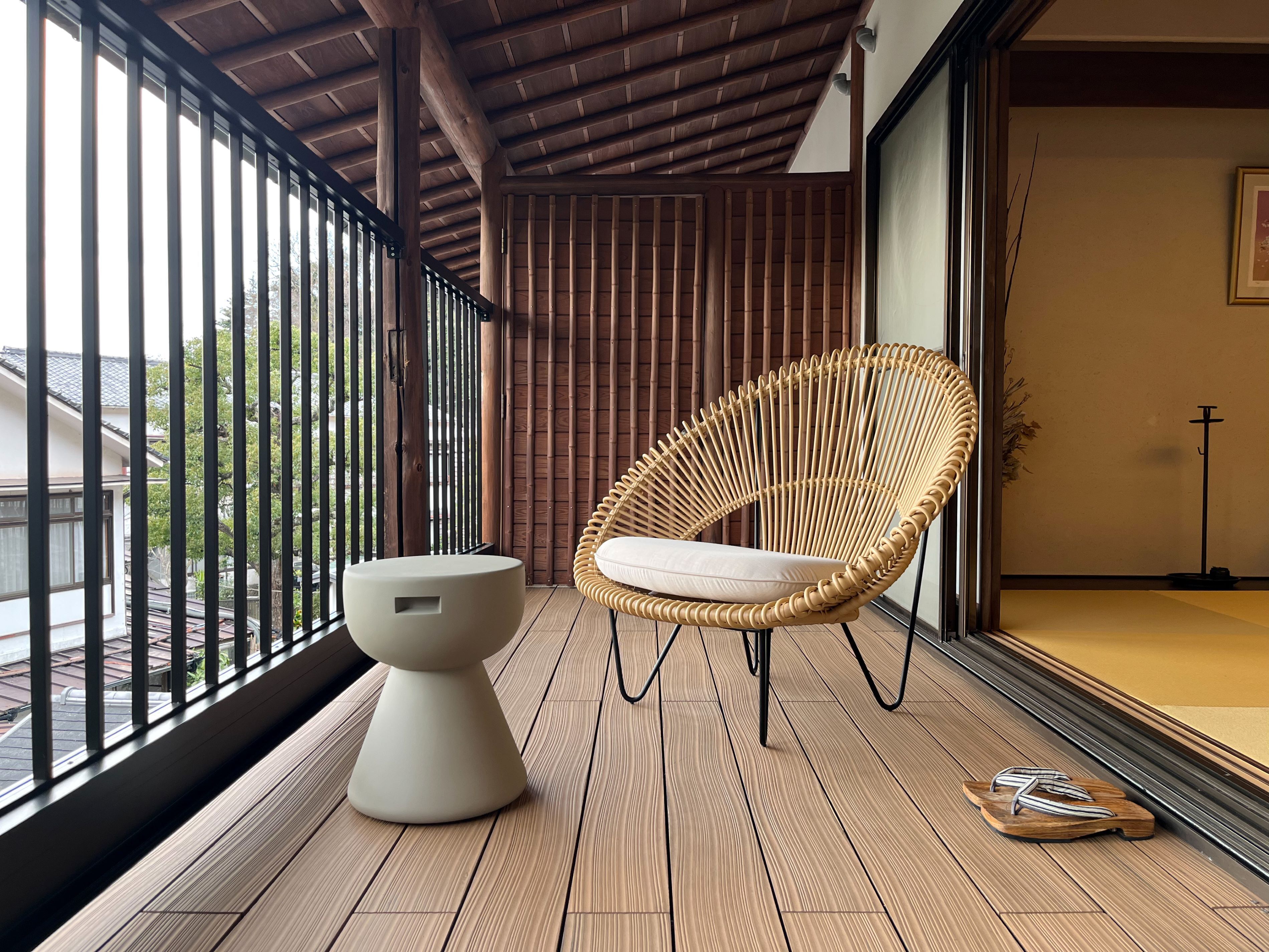 Ein Balkon mit Holzboden, einer weißen Toilette, einem Korbstuhl und einem Paar Sandalen.