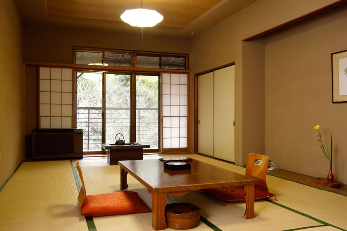 Ein traditioneller japanischer Raum mit Tatami-Böden, einem niedrigen Holztisch, einem Tee-Set und Schiebetüren.