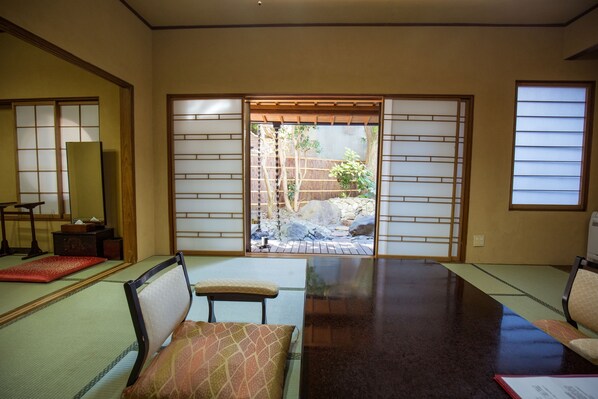 A traditional Japanese room with tatami flooring, a low table, and sliding doors leading to an outdoor garden.